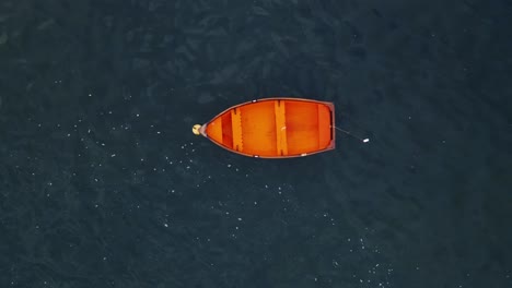 drone shot flying upwards from a small red boat in the middle of the ocean with no one inside it