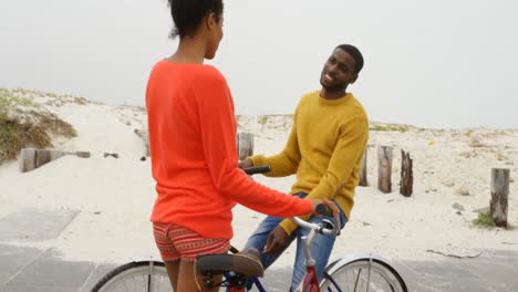 una joven pareja negra de pie con una bicicleta en la playa en un día soleado 4k