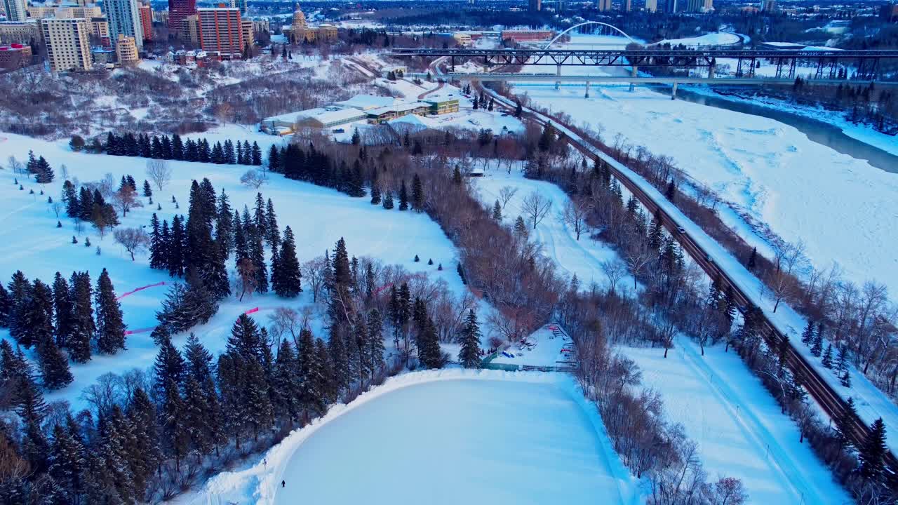 vista aérea de pájaro panout dolly rodar hacia abajo hacia arriba sobre la pista de patinaje sobre hielo artificial al aire libre más grande de canadá rodeada de pinos parque victoria con un puñado de personas patinando a menos 30c1-2
