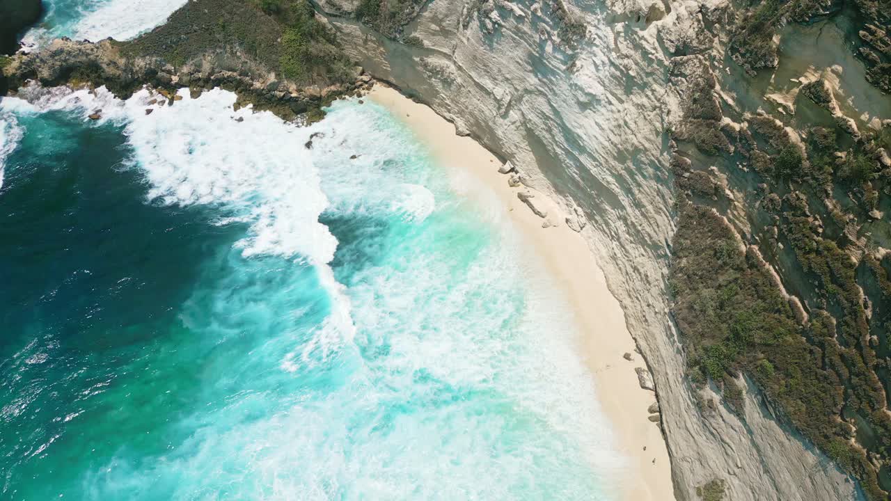 Static aerial view of surf and ocean waves on a small, sandy beach
