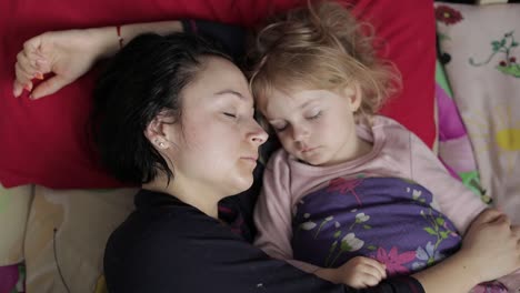 a woman and her young daughter sleeping together in bed