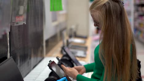 el primer plano de una bella mujer rubia mirando diferentes tabletas de computadora en la exhibición de una tienda