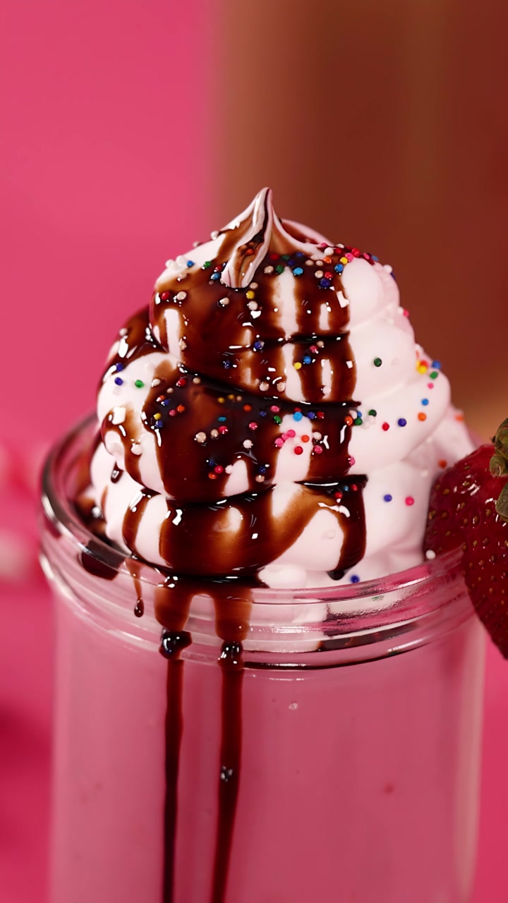 Sciroppo al cioccolato cola dalla panna montata con ciliegia su un frappè alla fragola, sfondo rosa vivace