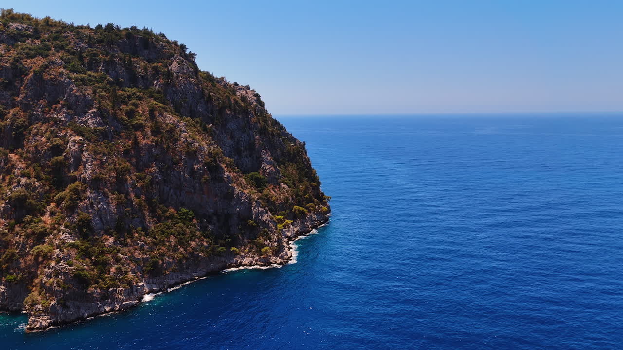 Unapproachable rocky shore washed by the azure sea water. Drone flight over the endless waterscape sparkling in the sun