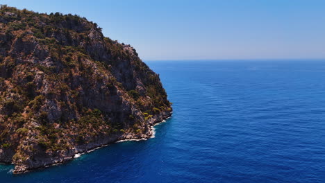 unapproachable rocky shore washed by the azure sea water. drone flight over the endless waterscape sparkling in the sun