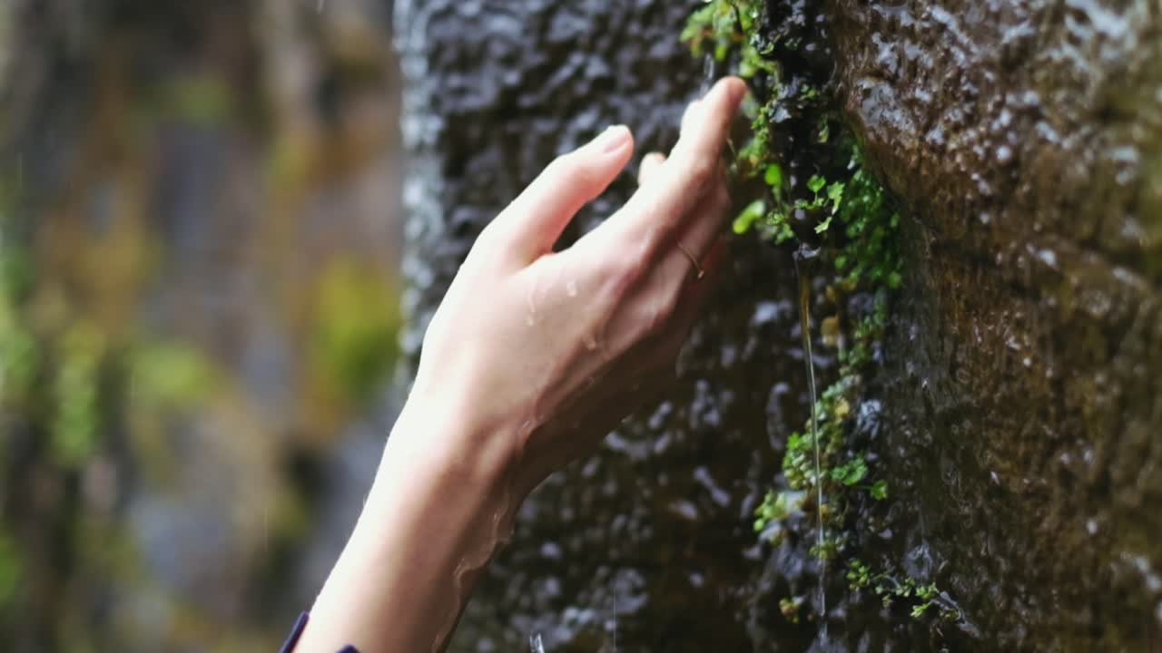 mano femenina, tocando y disfrutando de la naturaleza mientras la lluvia cae sobre su mano en cámara lenta
