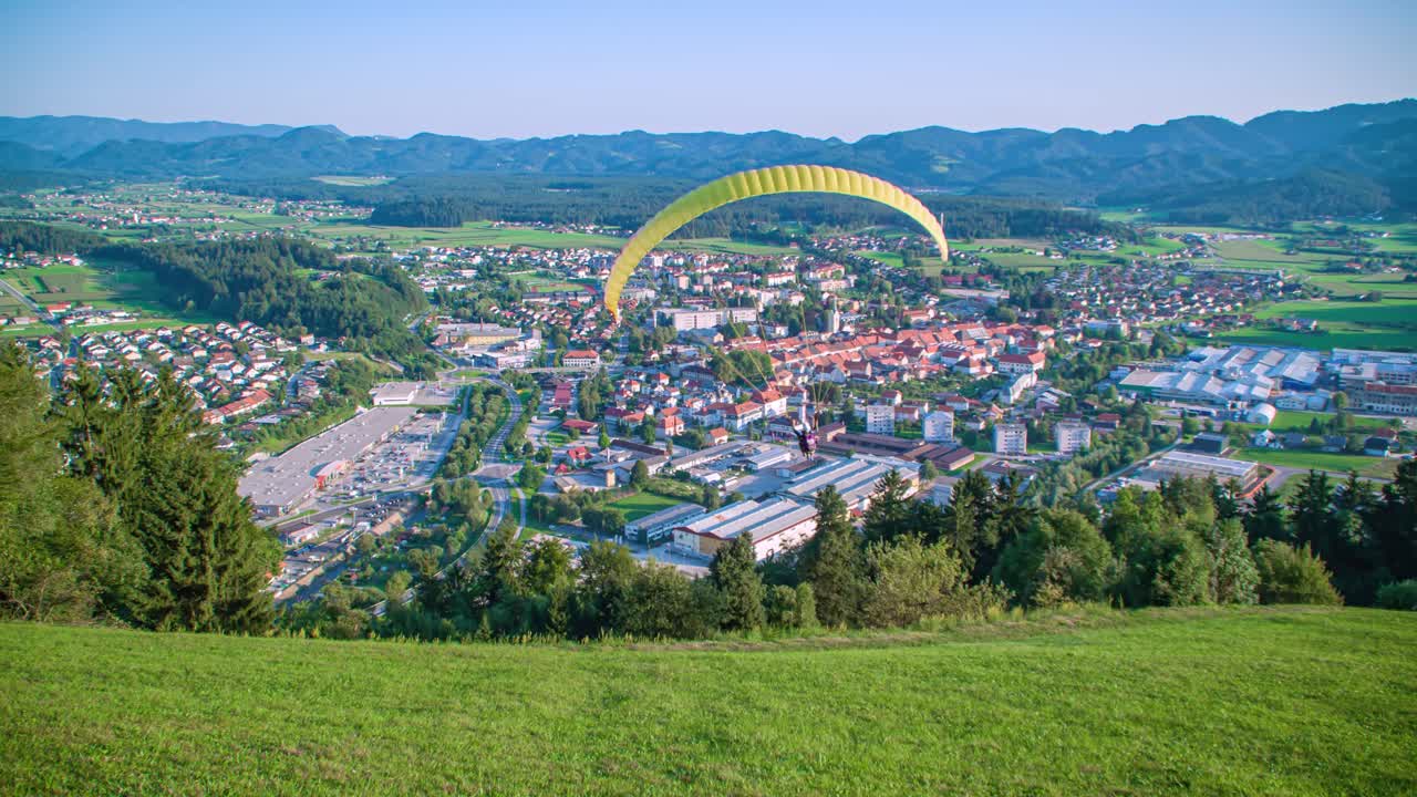 Parachute gliding smooth down the mountain over a cute little town. Slovenia