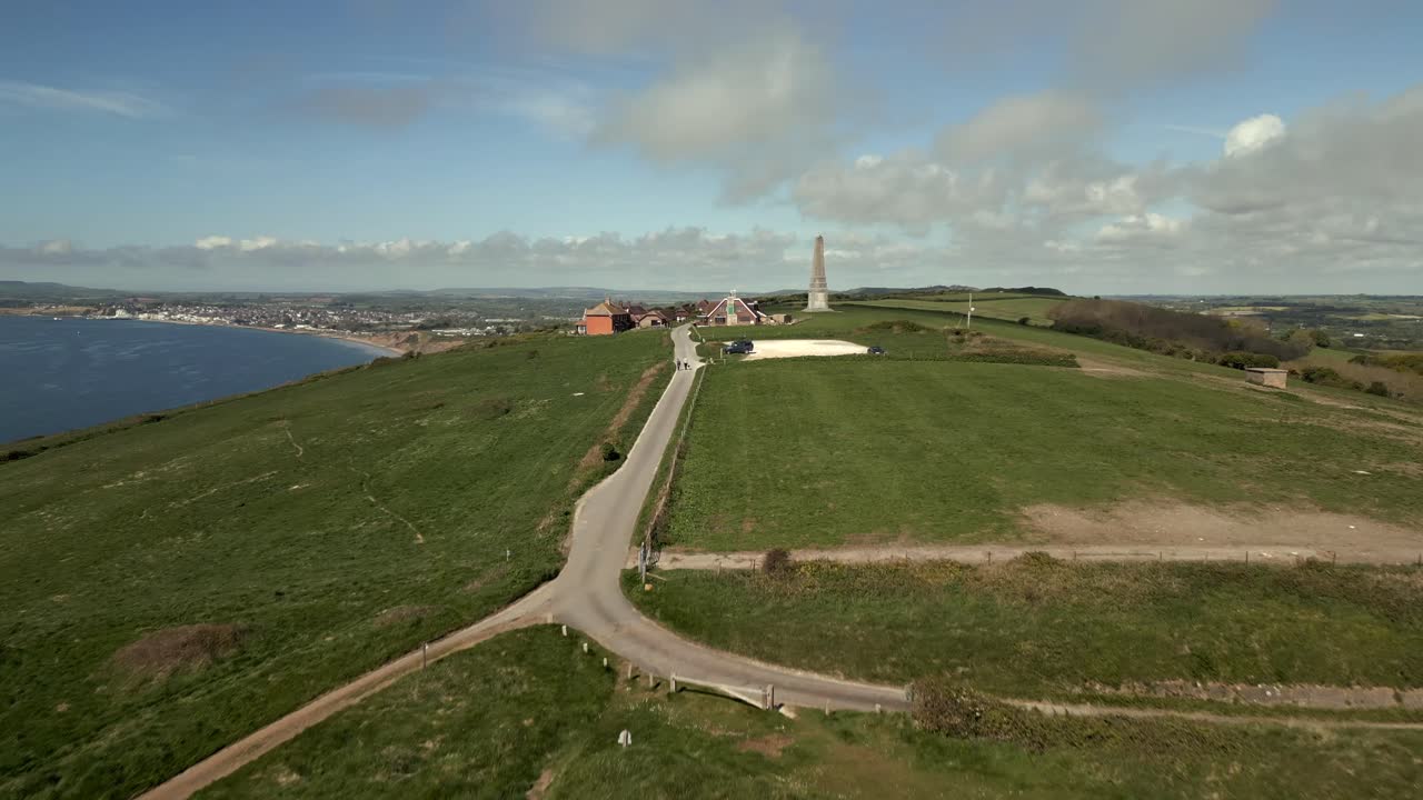 Rapid aerial push toward coastal monument on green hill above seaside town