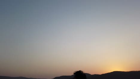 Junger-Mann-Sitzt-Auf-Einem-Felsen-Bei-Sonnenuntergang-über-Einem-Tal-Mit-Wunderschöner-Landschaft