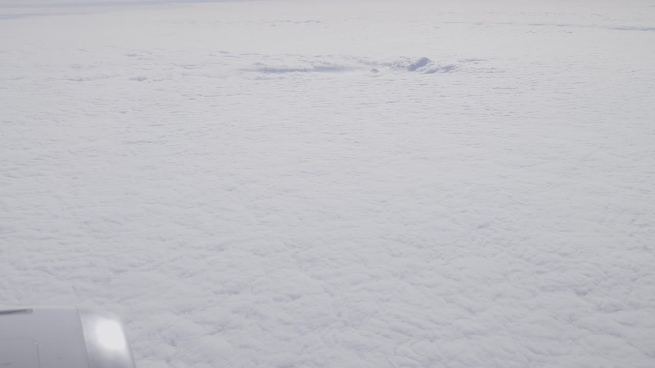 A cloud-covered sky with subtle light and an aircraft engine visible, aerial view