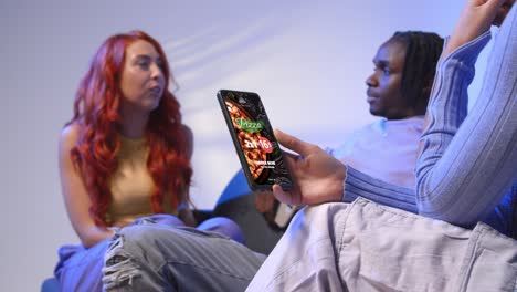 primer plano de una mujer con un menú de pizza en el teléfono móvil sentada con amigos de la generación z hablando