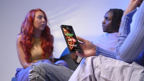 close up of woman with pizza menu on mobile phone sitting with gen z friends talking