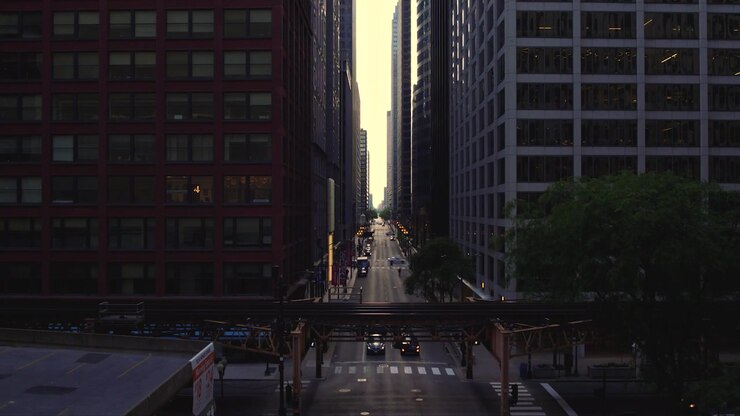 Vista drone su una strada del centro di Chicago sotto i binari sopraelevati della CTA, incorniciata da grattacieli, traffico, alberi e una calda luce serale