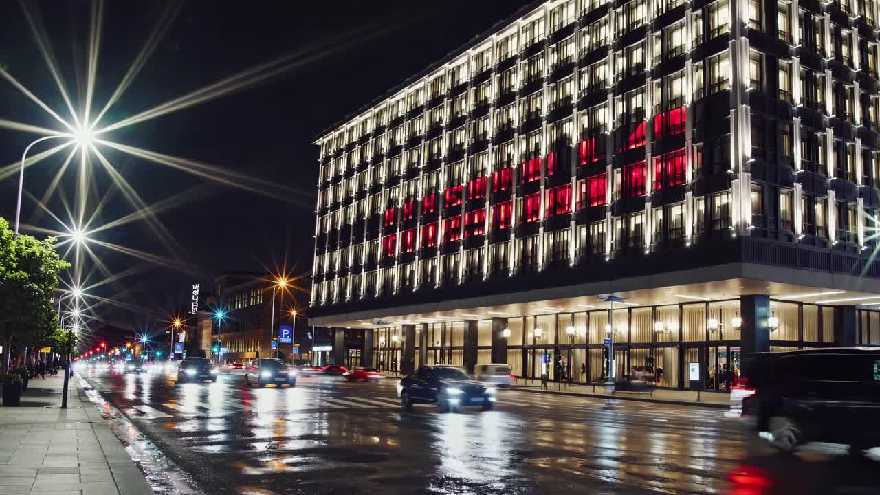 은 불빛으로 빛나는 호텔 전면, 은 도로 표면에 반사, 지나가는 자동차, 야간 도시 장면 동안 모션 블러를 만니다.