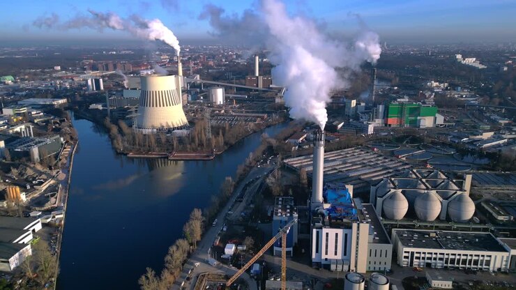 industrial heating plant with chimney releasing smoke into blue sky, impacting environment by a canal. Tremendous aerial view panorama overview drone