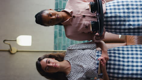 Vertical-Video-Of-Two-Serious-Female-Owners-Or-Staff-With-Digital-Tablet-And-Cups-In-Coffee-Shop