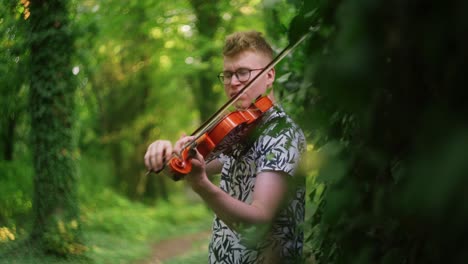 Soulful-violinist-plays-the-violin-in-a-dreamy-lush-green-forest,-handheld