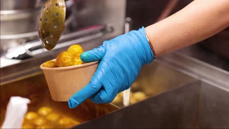 gloved hands serving meatballs into a bowl