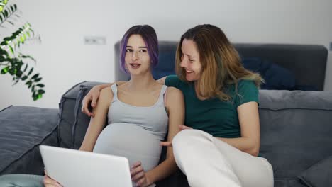 Happy-gay-pregnant-woman-using-laptop-computer-with-her-wife-on-sofa