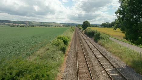 Aerial-view-of-British-rural-scene-with-train-tracks,-agricultural-farmland-and-green-fields