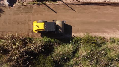 toma aérea de arriba hacia abajo de la máquina de nivelación rodante amarilla que trabaja en la carretera del sitio de construcción en un día soleado