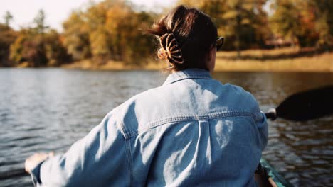 a woman wearing a denim shirt paddles a kayak on calm water, creating ripples as the paddle cuts through the surface