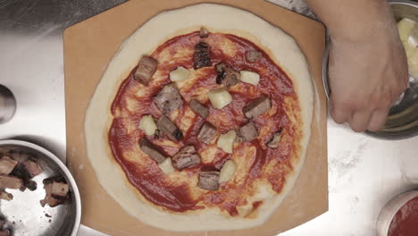 placing cubed cheese on pizza dough topped with meat and pizza sauce before baking