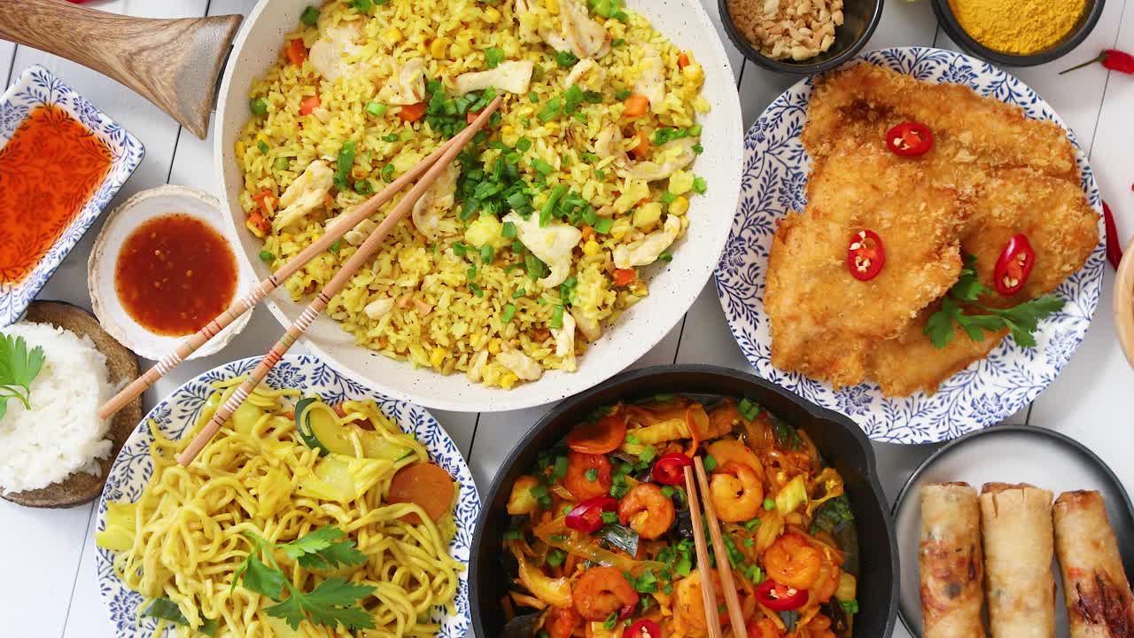 Makanan Asia disajikan. Piring, wajan, dan mangkuk penuh mi, tumis ayam, dan sayuran