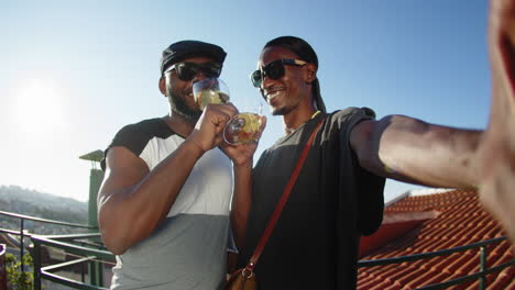 pov of happy gay in bandana taking photo with lover and clinking drinks on rooftop