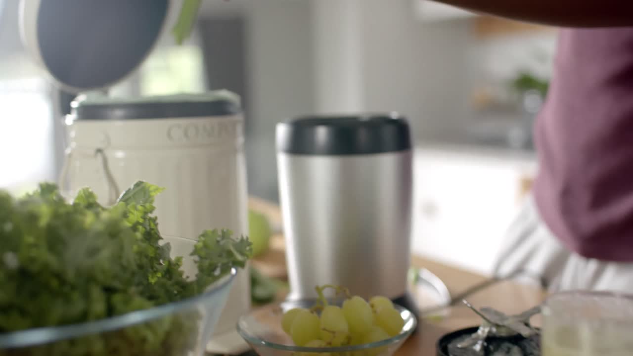 sección media de un hombre afroamericano limpiando residuos en la cocina en casa, cámara lenta