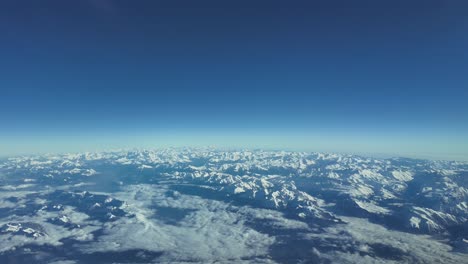 vista aérea de las montañas nevadas de los alpes tomada desde una cabina de un avión mientras vuela a través de un cielo brillante y azul