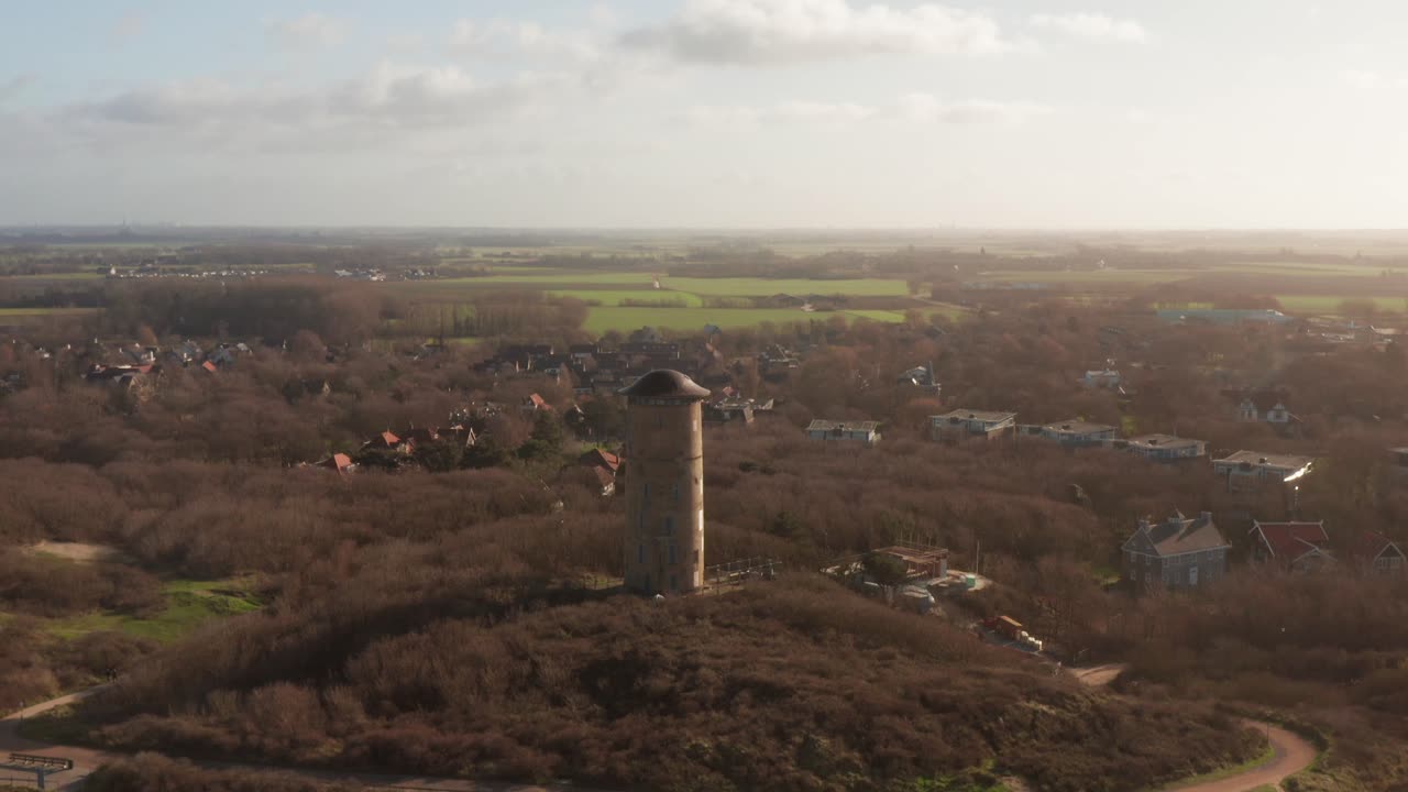Revealing drone shot of a water tower and the touristic village behind the dunes