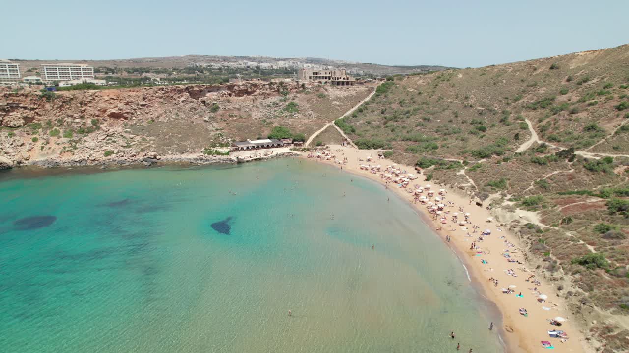 Beach with tourists sunbathing and swimming in Malta. Mediterranean Sea holiday destination