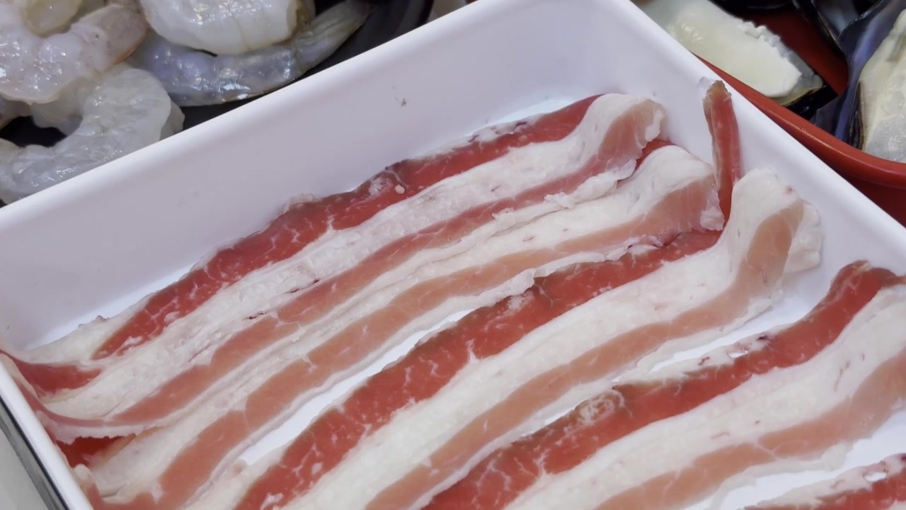 Close-up de carne bovina premium fatiada finamente, disposta em um prato de servir, preparada para shabu shabu com ingredientes frescos e apresentação elegante.