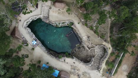 Cenote-zemway-in-tulum-with-crystal-clear-waters-surrounded-by-lush-greenery-and-sandy-areas,-aerial-view