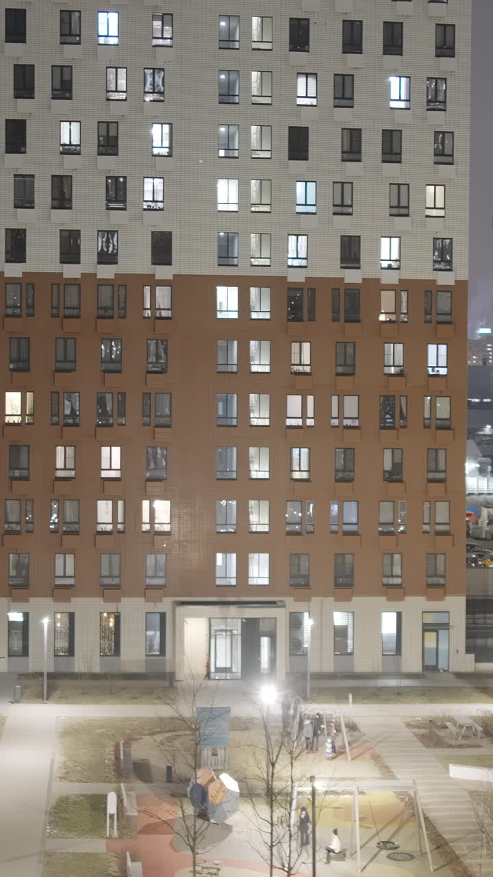 Modern Apartment Building at Night with Illuminated Windows and People Outdoors
