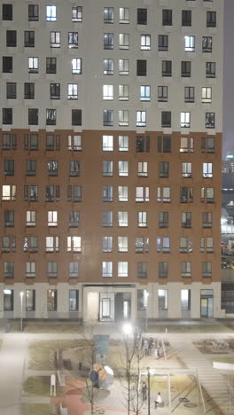 modern apartment building at night with illuminated windows and people outdoors