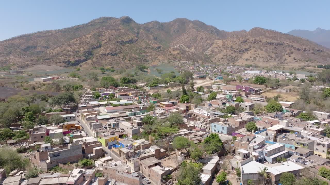 Blue agave agricultural fields in Jalisco Amatitan town, residential houses and rugged mountain landscape, establishing drone shot