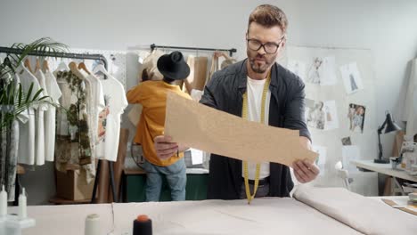 young designer takes measurements while a man and blonde woman colleagues choose clothes and then aproach to desk