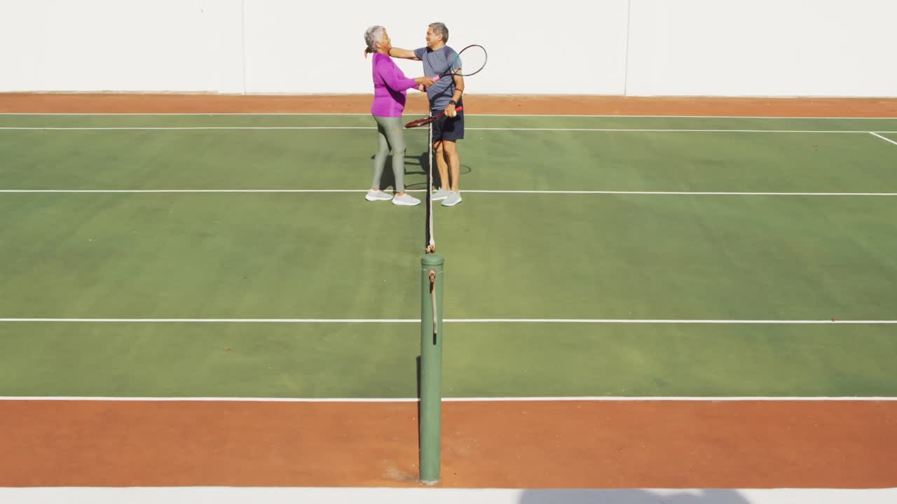 테니스 코트에서 경기 후 포옹하는 행복한 두 인종의 고령 커플의 비디오
