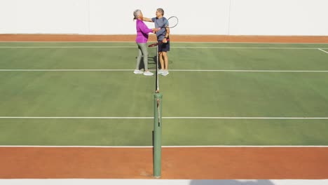 video of happy biracial senior couple embracing after match on tennis court