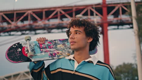 relaxed skater walking embankment portrait. curly guy crossing city vertical