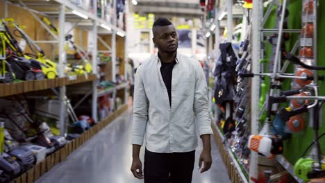 african american man walking along shelves in hardware store and examines goods