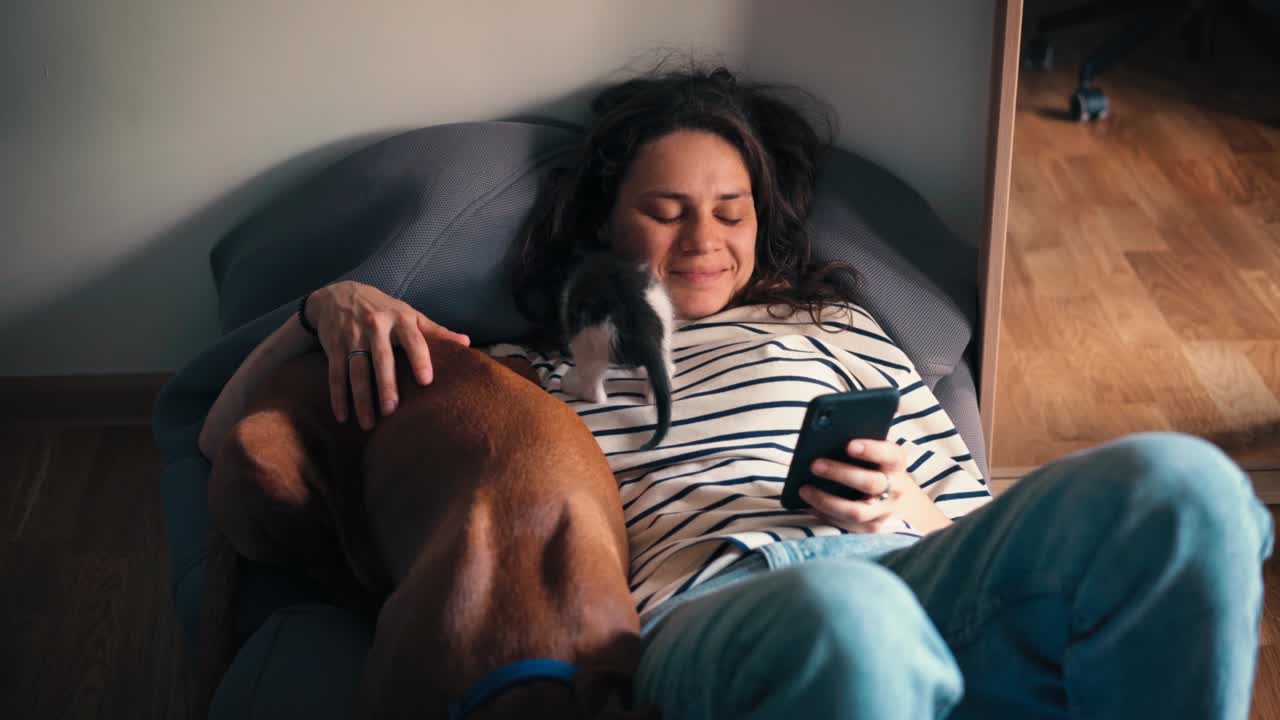 una mujer joven acostada en una almohada grande abrazando a su perro y un pequeño gatito