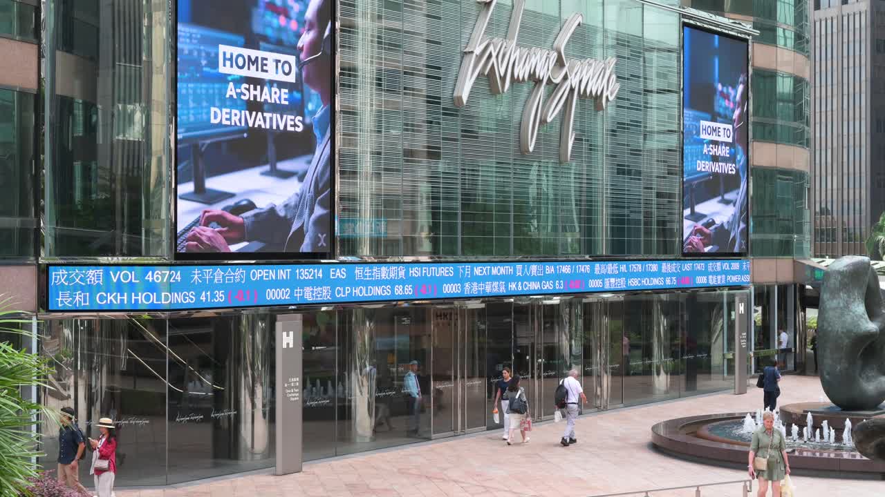 Professionals and pedestrians walk past a moving screen displaying stock ticker symbols at Exchange Square, home to the Hong Kong Stock Exchange (HKEX), in the financial district of Hong Kong, China.