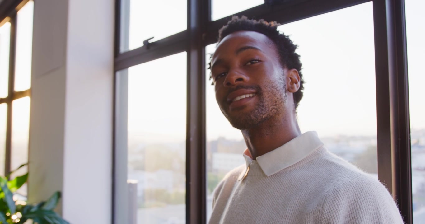 African American man holding tablet reading mail tapping looking out by sill turning to cam smiling