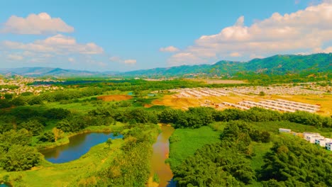 drone footage of gurabo river winding through lush trees beside community construction in puerto rico, filmed in late morning light. perfect for real estate, environment, and infrastructure visuals