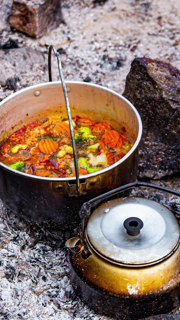 Timelapse stew cooking food being mixed over fire in metal pot with wood coals on sand floor