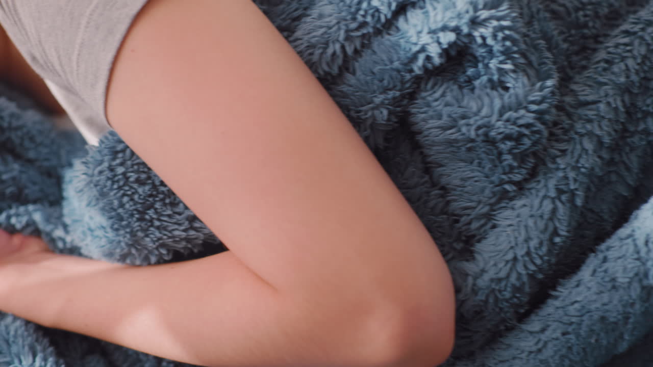 Close up of young girl snuggling under soft blue blanket while wiggling leg, creating gentle folds and textures, cozy indoor atmosphere symbolizing warmth