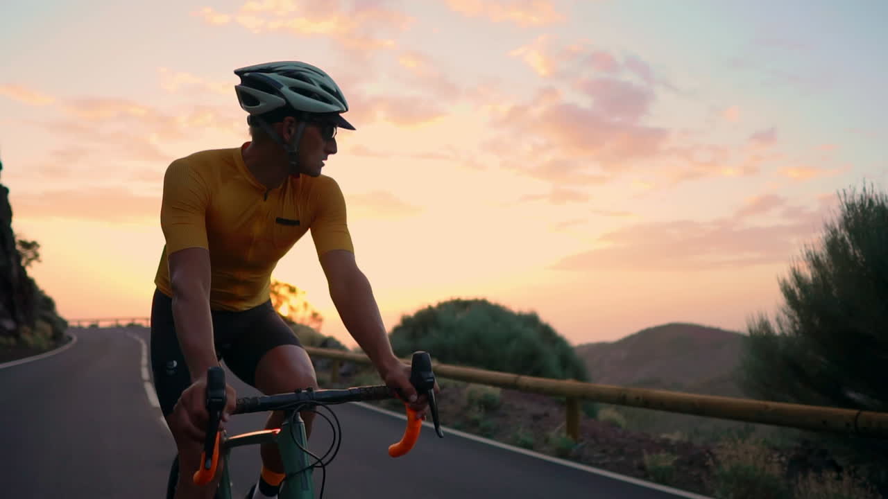 Slow motion captures the athlete cycling along a mountain serpentine on a bike, taking in the island's view, embodying dedication to a healthy lifestyle at sunset